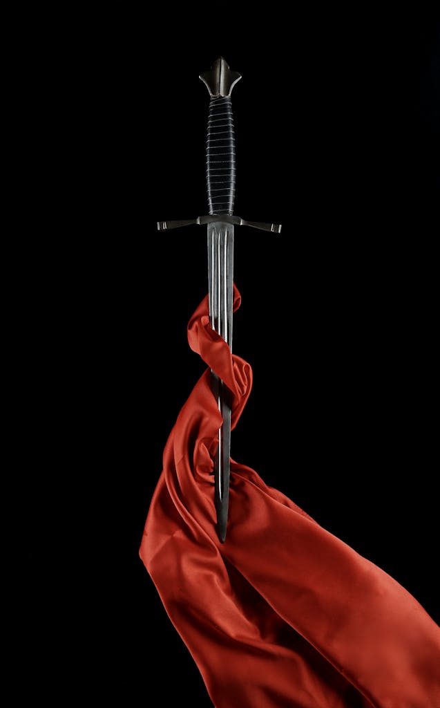 A striking still life of a medieval sword wrapped in red silk, set against a black background.